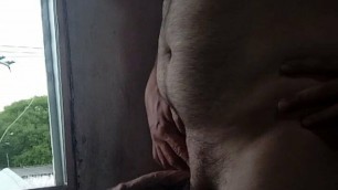 Mature man masturbating in front of window with the rain.